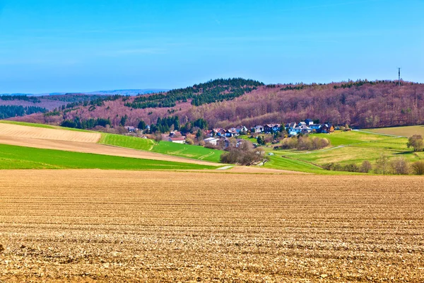 Paisaje con campos y un pueblo con colinas en el horizonte —  Fotos de Stock