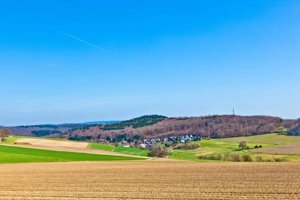 Landschaft mit Feldern und einem Dorf mit Hügeln am Horizont — Stockfoto