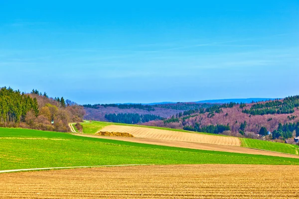Krajinu s poli a vesnice s kopce na obzoru — Stock fotografie
