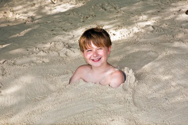 Menino feliz coberto por areia fina na praia — Fotografia de Stock