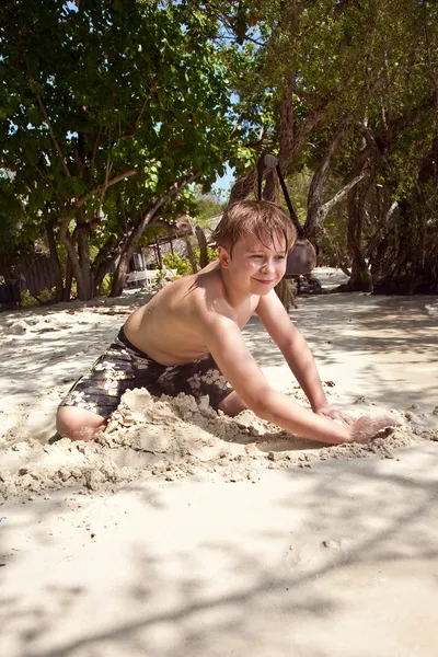 Szczęśliwy młody chłopak jest kopanie w piasku na plaży i konstruowanie — Zdjęcie stockowe