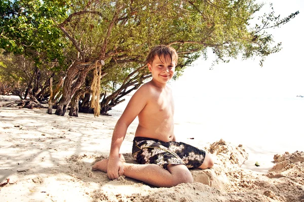 Niño feliz está cavando en la arena de la playa y construc —  Fotos de Stock