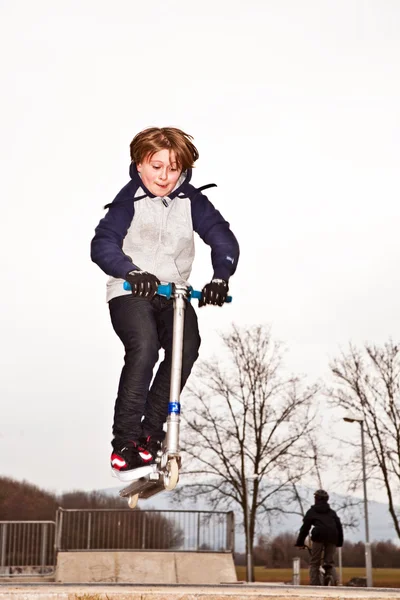 Rapaz a saltar com uma scooter sobre uma rampa — Fotografia de Stock