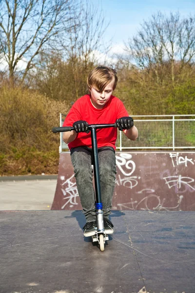Junge genießt Reiten mit seinem Roller und Springen — Stockfoto