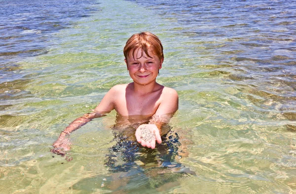 Menino no oceano mostra areia limpa em sua mão — Fotografia de Stock