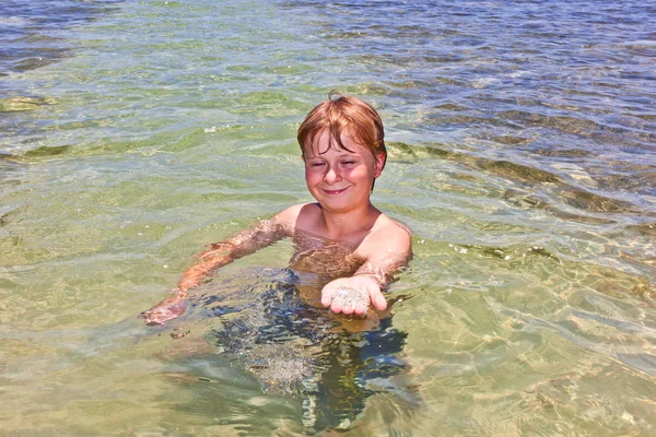 Chico en el océano muestra arena limpia en su mano — Foto de Stock