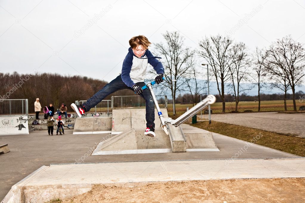 Boy jumping with a scooter over a ramp