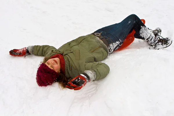 Flickan liggande i snön från pulka ner för backen i vinter — Stockfoto