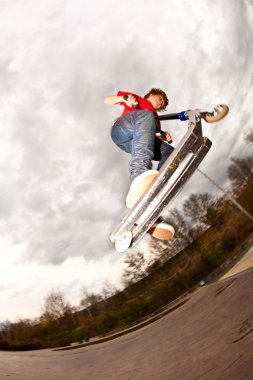 Young boy enjoys riding a scooter in the skate park clipart