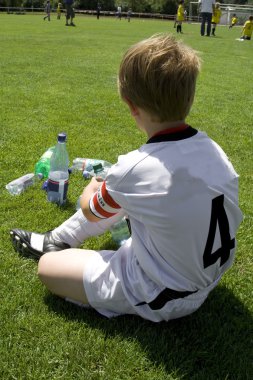 Exausted boy takes a rest in the halftime of a football match clipart