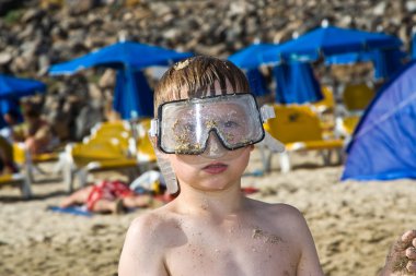 Child, boy with diving goggles is playing intensively at the sandy beach clipart