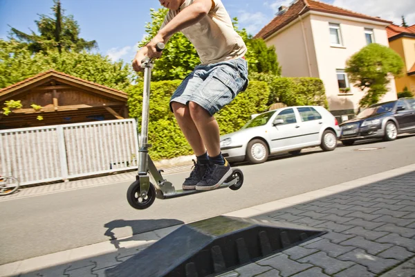 Menino montando uma scooter indo para o ar — Fotografia de Stock