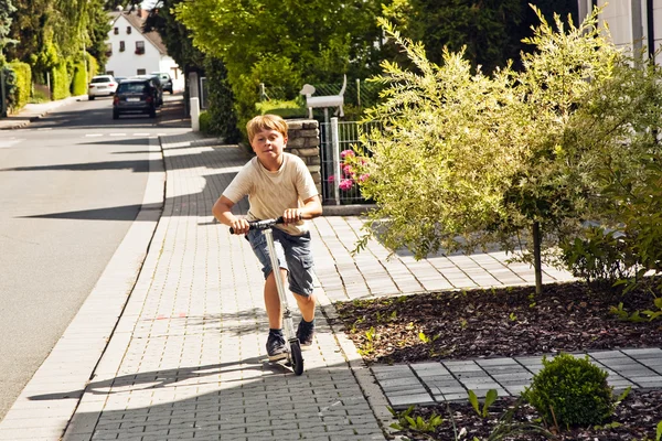 Garçon promenades scooter sur le pavé à une rue — Photo