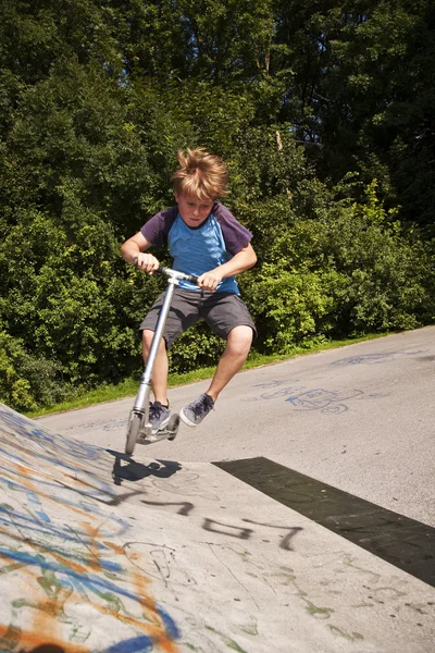 Menino tem divertido scooting no scating no skatepark — Fotografia de Stock
