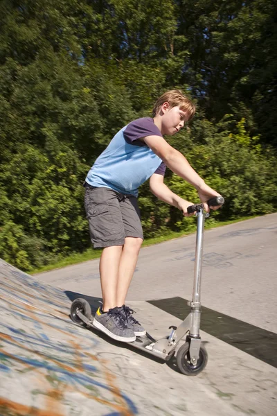 Мальчик катается на скутере по трубе в скейт-парке — стоковое фото