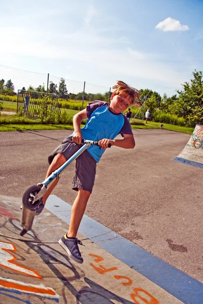 Pojken har kul scooting i scating på skatepark — Stockfoto