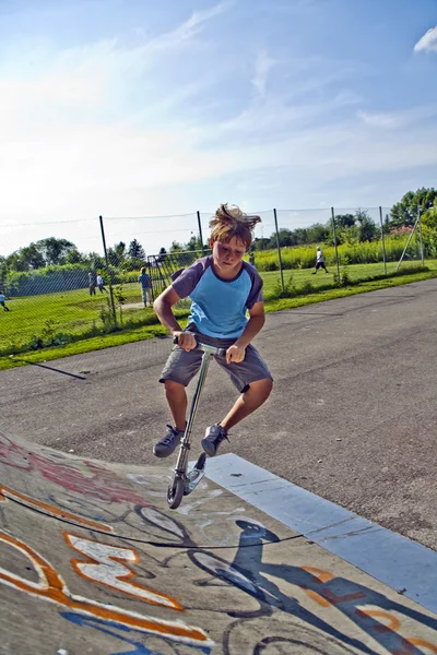 Chłopiec jeździ na skuterze w rurze w skate parku — Zdjęcie stockowe