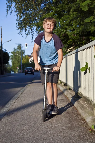 Menino monta scooter no caminho na área pública — Fotografia de Stock
