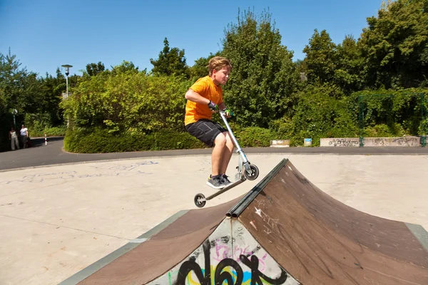 Chico está saltando con un scooter sobre una espina dorsal en el skate parc y —  Fotos de Stock