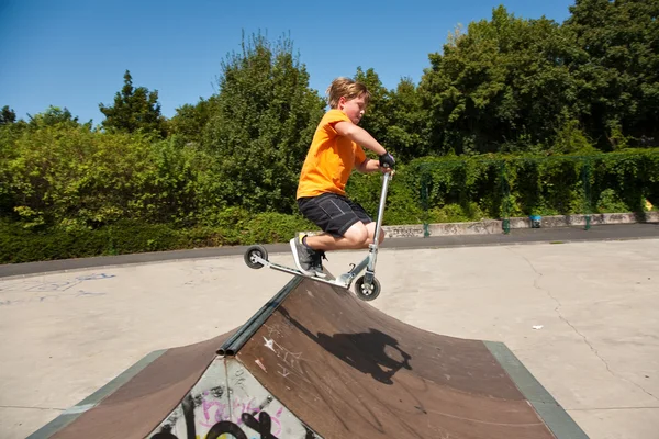 Chico está saltando con un scooter sobre una espina dorsal en el skate parc y —  Fotos de Stock
