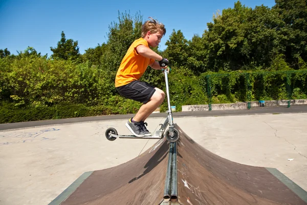 Pojken hoppar med en skoter över en ryggrad i skate parc och — Stockfoto