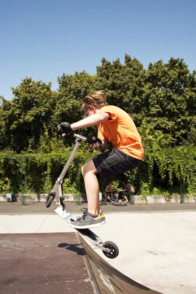 Menino está pulando com uma scooter sobre uma coluna vertebral no parc skate e — Fotografia de Stock
