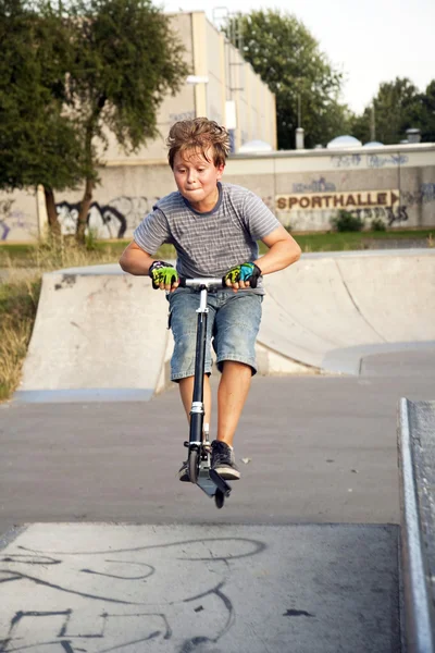 Pojken hoppar med en skoter över en ryggrad i skate parc och — Stockfoto