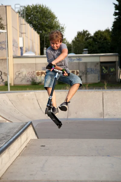 男孩用滑板车跳过在滑板公园的脊椎和 — 图库照片