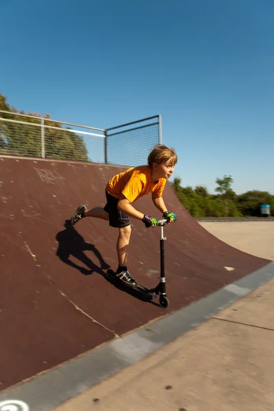 男孩用滑板车跳过在滑板公园的脊椎和 — 图库照片