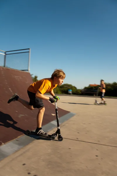 Chico está saltando con un scooter sobre una espina dorsal en el skate parc y — Foto de Stock
