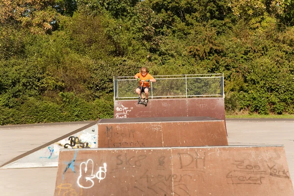 Garçon saute avec un scooter sur une colonne vertébrale dans le skate parc et — Photo