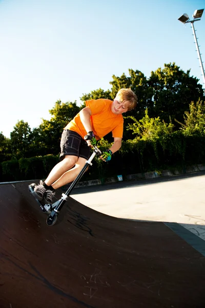 Niño con scooter y camiseta naranja está haciendo trucos en la sca — Foto de Stock