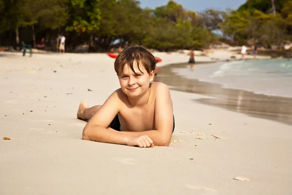 Rapaz feliz deitado na praia — Fotografia de Stock
