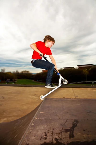 Ung pojke har ridning en skoter i skateboardpark — Stockfoto