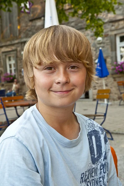 รูปภาพของเด็กชายที่มีความสุขที่ยิ้ม นั่งอยู่ในร้านอาหารกลางแจ้ง — ภาพถ่ายสต็อก