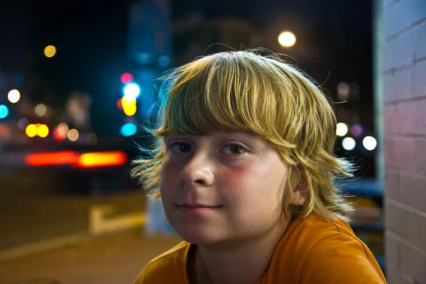 Schattige jongen glimlacht moe zittend buiten per nacht — Stockfoto