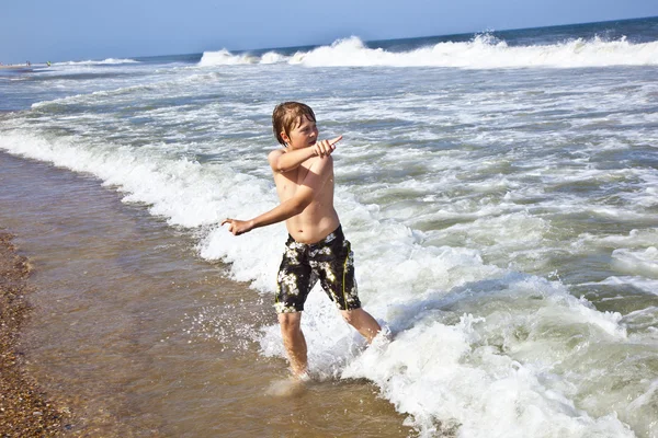 年轻的男孩在海滩上通过水运行 — 图库照片
