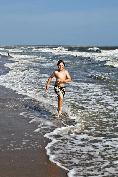 Menino correndo pela água na praia — Fotografia de Stock