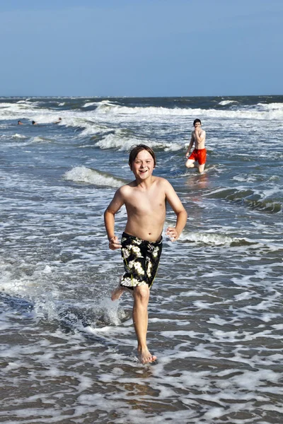 年轻的男孩在海滩上通过水运行 — 图库照片