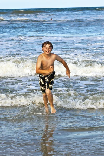Jeune garçon courant dans l'eau à la plage — Photo