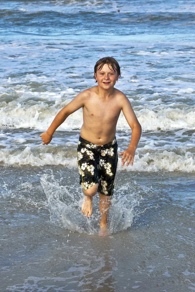 Mladý chlapec běží ve vodě na pláži — Stock fotografie