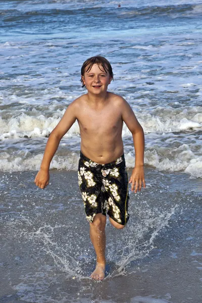 Jeune garçon courant dans l'eau à la plage — Photo