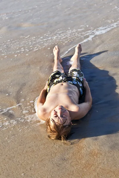 Menino deitado na praia e desfrutando do oceano — Fotografia de Stock