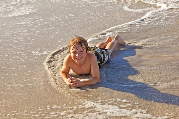 Niño acostado en la playa y disfrutando del océano — Foto de Stock