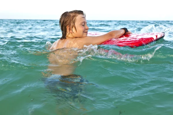 Симпатичный мальчик с доской для серфинга в море — стоковое фото