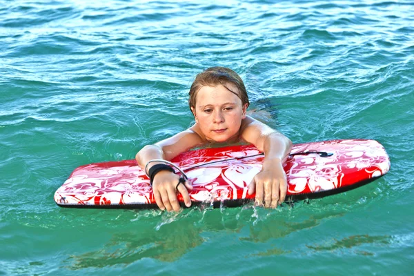 Lindo chico con tabla de surf en el mar —  Fotos de Stock