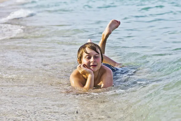 Garçon aime se coucher sur la plage dans le surf — Photo