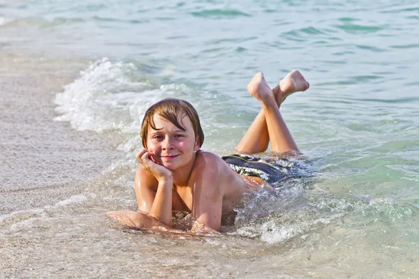 Chlapec se těší, ležící na pláži v příboji — Stock fotografie