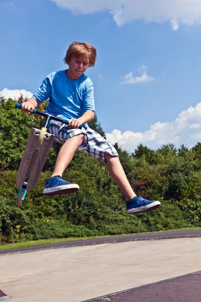 Młody chłopiec będzie latał ze swoim skuterem. — Zdjęcie stockowe