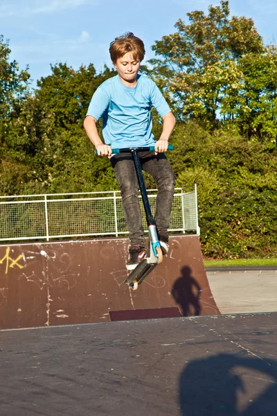 Chłopiec skacze z skuter w skate parku na ziemi — Zdjęcie stockowe